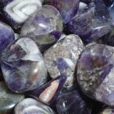 a close up of banded amethyst tumblestones. Rich deep purple with bands and chevrons of white and pale grey