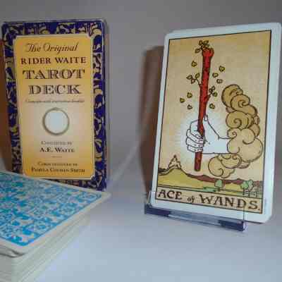 the rider-waite deck, showing the box design, the corner of the card pack to see back of card, and the ace of wands card - a hand coming out of a cloud and holding a flowering staff