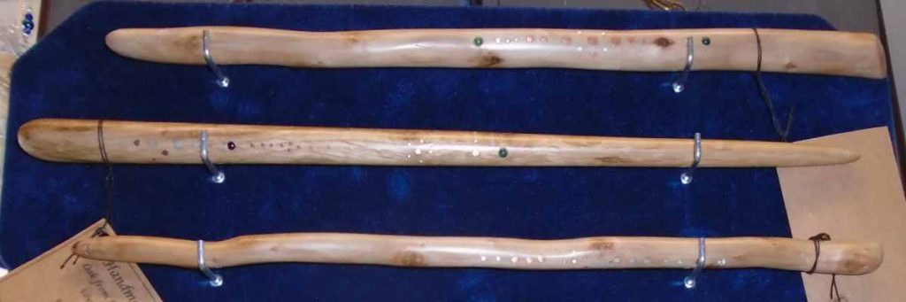 3 handcrafted wooden wands with gemstone and metal inlay on blue velvet background