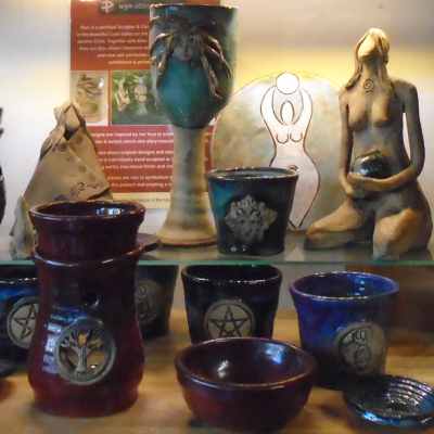 A selection of pottery by Wyn Abbott Ceramics, featuring a Green Lady Goblet, 3 small pots with pentacle, green man and goddess designs and oil burner with tree of life design, a goddess plaque and a small shaman figurine